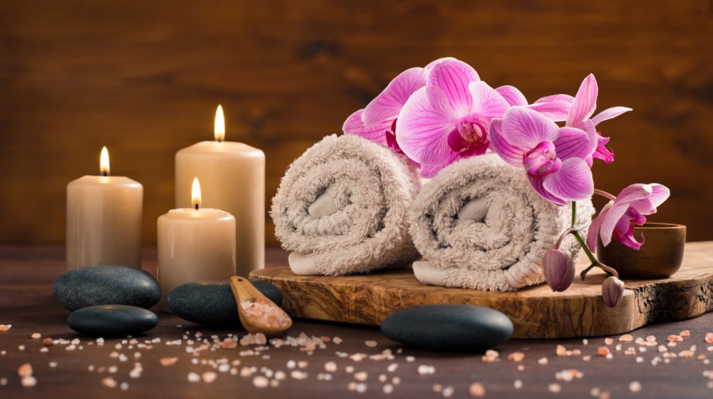 spa-setting-with-brown-rolled-towel-orchids-candles-wood